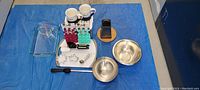 Photo showing assorted kitchen ware items arranged on blue tarp including Pyrex glassware, stainless steel bowls, kitchen tools, mugs, and grater.
