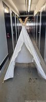 Front view of the children's tee pee, showing white canvas entrance and wooden poles crossing at the top inside a hallway with lockers on both sides.
