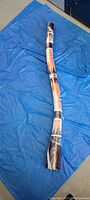 Full length of the Australian didgeridoo laid on a blue tarp showing painted decoration and natural wood finish.