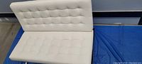 Front view of white faux leather two seater couch highlighting tufted seat and back cushions.