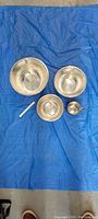 Full view of all four items laid on blue fabric: three nesting bowls in decreasing sizes and one cup