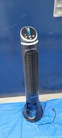 Full view of the black Honeywell Quiet Set tower fan standing against a blue background, power cord visible.
