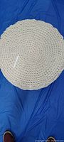 Top view of the round woven ottoman on a blue background, showing the circular knit pattern and texture.