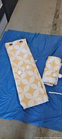 Two curtain panels laid flat showing yellow and white geometric pattern and rope tiebacks tied around one panel.