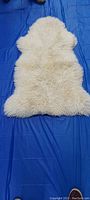Photo showing the full view of the cream-colored small faux throw rug laid out on a blue surface.