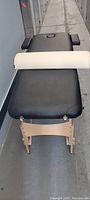 Top side view of therapy table covered with black pleather, showing wooden legs and cream-colored roll cushion placed on it