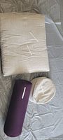 Three meditation cushions laid out: one rectangular beige linen cushion, one round beige linen cushion, and one dark purple cylindrical bolster cushion.