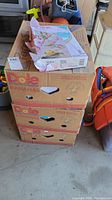 Stack of three large cardboard boxes, two are Dole banana boxes with holes, top box is worn Xerox pastel art paper box