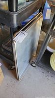 Two large metal commercial baking sheets leaning against a utility cart, showing corners and edges with some wear.