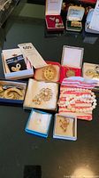 Photo of assorted costume jewelry including brooches, earrings, and necklaces displayed in open boxes and on a tabletop.