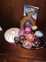 Hand painted decorative eggs in a dark dish, white decorative jar with red detail, wooden plaque with traditional design.
