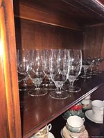 Crystal stemware including wine glasses, champagne coupes, and other tall glasses with star cut design on stems, arranged on dark wood shelf