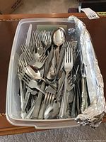 Plastic bin full of assorted forks, spoons, and knives, showing mixed designs and patterns.