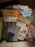 Overall collection of children's educational books stacked in a box, showing colorful covers related to seasons, rainforest, African folktales, and other topics.