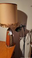 Photo showing artisan ceramic table lamp with fabric shade and fringe on wooden surface next to chrome floor lamp.