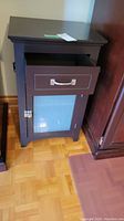 Front view of the dark brown composite board night table showing drawer and glass cabinet door.