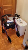 Overview of walker with seat and storage, commode chair, grab bar attached to hamper and medical boxes on hamper lid.