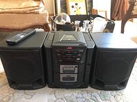 Full front view of the JVC portable stereo system with two attached speakers and remote on top