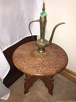 Side table with carved floral and leaf patterns, topped with brass oil pitcher