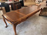 Angled side view showing the full length, curved edges, graduated colors and detailing on the top surface, cabriole legs.