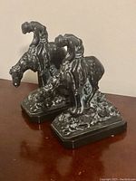 Pair of monochrome Ronson Metal Works 'End of Trail' bookends showing a Native American man resting on his horse, viewed from an angle on a wooden surface.