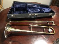 Disassembled bell and outer slide laid beside open hard case on wood surface