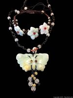 Overview of carved jade butterfly pendant necklace laid next to carved jade flower bracelet with beaded woven cords.