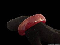 View of cherry amber Bakelite bangle on black display stand showing smooth rounded surface and reddish tone.