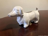 Side front view of vintage concrete dachshund garden statue showing shape, texture, and surface wear.