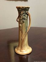 Front-right angle view of early 20th century Weller vase showing apple leaves and textured woodblock design with tall slender profile and handle shaped like a vine branch.