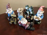 Photo showing six vintage garden figurines including three garden gnomes, bird, frogs, and dog on tricycle with visible wear and broken eye on frog figurine