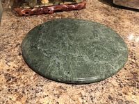 Top view of a smooth, round green marble hot plate against a granite countertop.