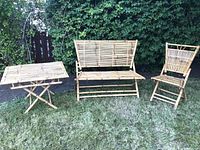 Photo of vintage 1960s bamboo tiki patio furniture set outdoors on grass showing the table, loveseat, and chair spread out.