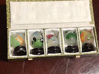 Top view of box open showing five miniature inside-out painted glass eggs on black stands inside cloth lined compartments