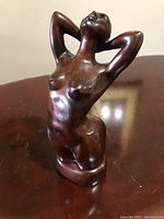 Close-up front view of bronze nude female statue, showing detailed form and polished surface.