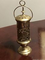 Front angle showing the pierced brass incense burner, highlighting its perforated sides, ornate rounded base, lid with ventilation holes, and carrying handle