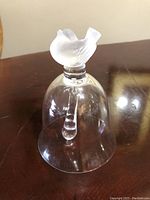 Photo of clear crystal bell with frosted bird handle from front view on dark wood surface.