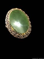 Front view of the oval-shaped green jade cabochon brooch set in a sterling silver decorative frame with scroll filigree.