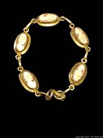 Full view of the vintage 12k gold filled cameo panel link bracelet laid flat on black background showing five oval carved cameo panels.