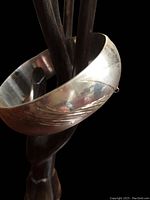 Close-up of vintage sterling silver bangle bracelet with etched design, displayed on a hand sculpture, showing missing safety chain loop.