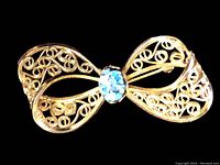 Full view of the bow-shaped brooch showing gold-filled filigree loops and central opal stone.