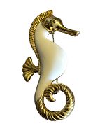 Front view of the gold tone and white enamel seahorse brooch showing detailed texture and design.