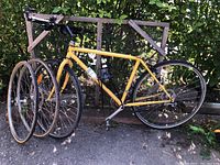 Yellow Schwinn road bike frame with three extra wheels leaned against fence outdoors