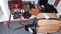 Full lot including vintage cameras, flash unit, camera bags arranged on floor showing all items.
