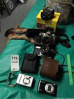 Overview of all lot items including cameras, flash unit, binoculars, cases, and packaging