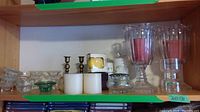 One shelf holding a variety of candles, candle holders, candlesticks, and glass containers.