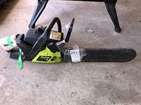 Full side view of Poulan chainsaw resting on concrete floor, showing body, handle and chain cover with sticker.