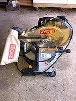 Front angled view of Ryobi chop saw showing dust bag attached to the saw arm and base.