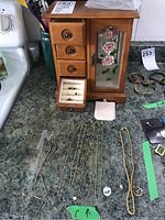 Full view of wood veneer jewelry box with floral glass door and several pieces of costume jewelry spread in front including rings and bracelets.