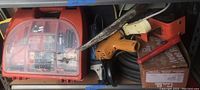 Shelf containing a Black & Decker cordless drill case with battery and bits, large hand saw, electric drill, red bolt cutter, and other tools.